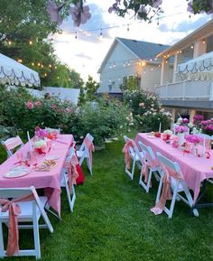 an outdoor dining area with pink and white table cloths, chairs, and lights