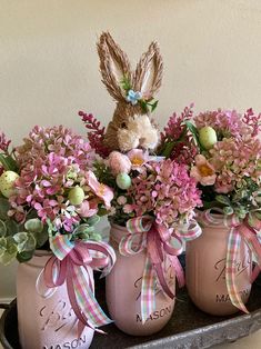 three mason jars filled with pink flowers and an easter bunny sitting on top of them