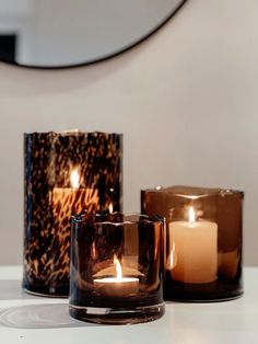 three candles sitting on top of a white table next to each other in front of a mirror