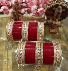 two red colored bangles with white stones on them sitting on a table next to pink flowers