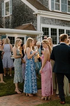 a group of people standing around each other in front of a house with wine glasses