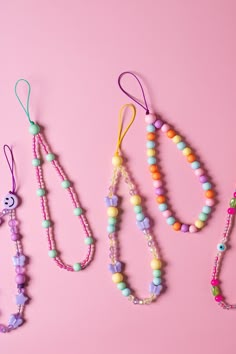 three necklaces are lined up on a pink surface, one is colorful and the other has beads