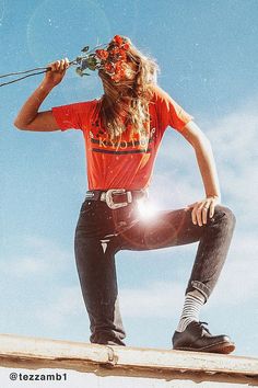 a man with long hair sitting on top of a wooden pole holding a flower in his mouth