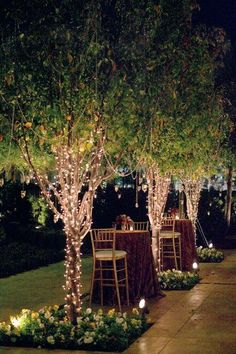 an outdoor dining area is lit up with fairy lights and decorated trees for the reception