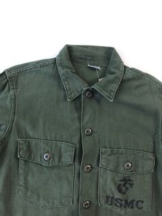 "USMC green cotton shirt circa 1971 has 'USMC' along with a globe screen printed on the chest pocket. The shirt has a button front, and cuffs, and chest pockets with buttoned flaps. Condition Overall excellent. Has some fade from wear near the back hem, a small stain near the button placket, and a tiny hole on the right arm near the shoulder. Measurements Chest 40\" Waist 38\" Shoulder 16.5\" Sleeve length 21.5\" Length 28\" Best for a size small." Green Button-up Shirt With Patch Pockets, Classic Green Shirt With Pockets, Green Long Sleeve Tops With Flap Pockets, Green Work Shirt With Patch Pockets, Cotton Long Sleeve Camp Shirt With Button Closure, Green Workwear Tops With Flap Pockets, Green Tops With Flap Pockets For Work, Classic Cotton Camp Shirt With Patch Pockets, Green Button-up Top With Patch Pockets