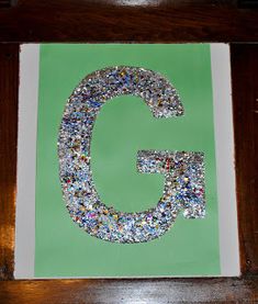 the letter g is made up of small pieces of silver and green paper with glitter on it