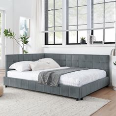 a large bed sitting on top of a wooden floor next to a white rug and window