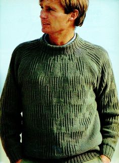 a man in a green sweater is standing with his hands in his pockets and looking off to the side