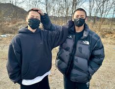 two men wearing face masks standing next to each other in front of some bare trees