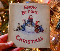 someone holding up a book in front of a christmas tree with snow before christmas written on it