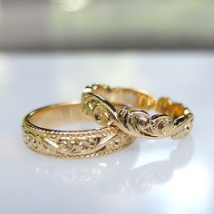 two gold wedding rings sitting on top of a white table next to each other,