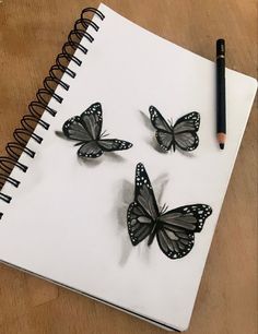 three butterflies sitting on top of a white notebook next to a black marker and pencil