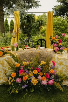 a table set up with yellow drapes and floral centerpieces for an outdoor dining area