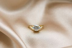 a diamond ring sitting on top of a white satin material with a gold tone finish