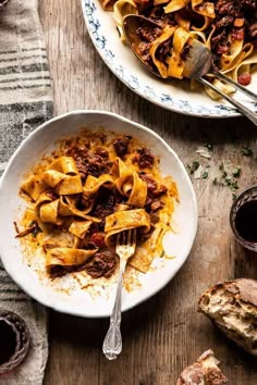 a bowl of pasta with meat and sauce next to a plate of bread on a wooden table