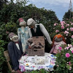 three scarecrows are sitting at a table in the garden