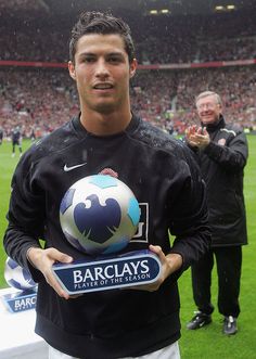 a man holding a soccer ball on top of a lush green field with people in the background