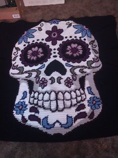 a crocheted skull with flowers on it's head sitting on the floor