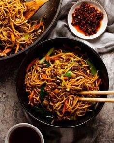 two pans filled with noodles and meat on top of a table next to chopsticks