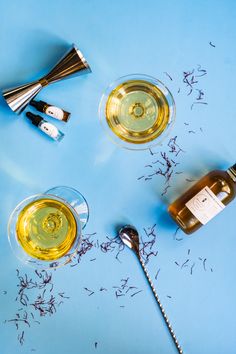 three wine glasses and two spoons on a blue surface with dried flowers around them