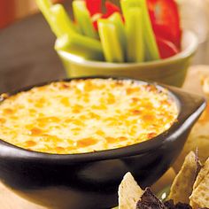 a bowl of cheese dip with tortilla chips and celery in the background