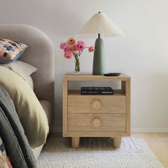 a nightstand with flowers on it next to a bed