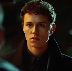 a young man in a black coat looking at the camera with an intense look on his face