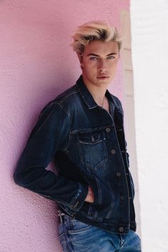 a young man leaning against a pink wall