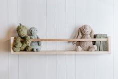 three stuffed animals sitting on top of a wooden shelf next to bookshelf against a white wall