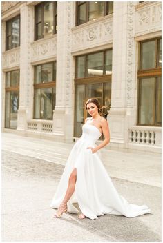 a woman is posing in front of a building wearing a white dress and high heels