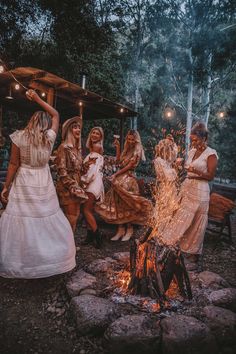 women in dresses dancing around a campfire at night with lights on their heads and arms