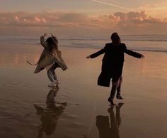 two girls running on the beach at sunset with their arms outstretched and one girl holding an umbrella