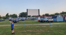 a group of people standing in front of a movie screen on top of a grass covered field