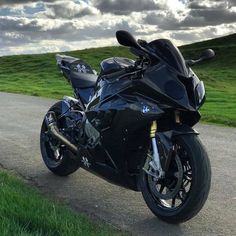 a black motorcycle parked on the side of a road next to a lush green field