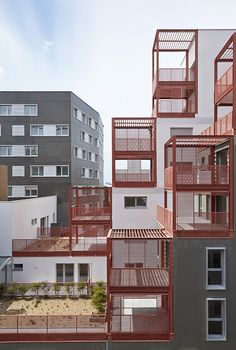 an apartment building with red balconies on the top and bottom floors, in front of other buildings