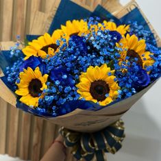 a bouquet of sunflowers and blue flowers is held by someone's hand