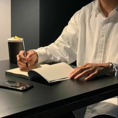 a man sitting at a desk writing on a notebook and holding a pen in his hand