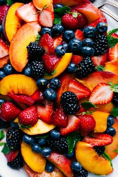 fresh fruit salad with peaches, blueberries and raspberries on a white plate