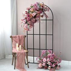 a chair sitting next to a floral arch with candles and flowers on the floor in front of it