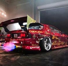 a red car parked in a garage next to another car with its hood open and lights on