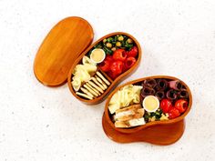 two wooden bowls filled with food on top of a white counter next to each other