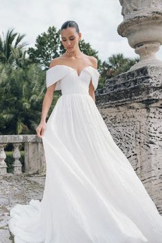 a woman in a white wedding dress standing on a stone wall with palm trees behind her