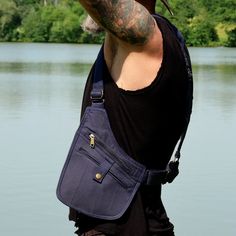 a man with tattoos on his arm holding a blue bag over his shoulder and looking at the water