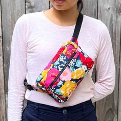 a woman wearing a white shirt and blue pants is holding a colorful floral bag in front of a wooden fence