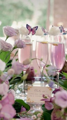 three glasses filled with pink liquid sitting on top of a table next to purple flowers