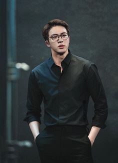 a man in black shirt and pants standing with his hands on his hips while wearing glasses