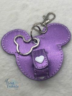 **Please Note** The white heart located where the key ring is, will not be white. It will be a silver metal color. This does not affect the white heart on the snap tab area.  Where do you stick your Mouse Ears when you are over wearing them at the park? Do you shove them in your backpack and risk ruining them? No way! Do you just tough it out and keep wearing them? Now you don't have too! This nifty keychain just hooks on to your backpack or purse and whenever you need a break from wearing your ears, you just snap them on the keychain and let them just hang. You also free up some space in your bag!  The keychain is made from a purple shimmer faux leather and comes with an adjustable to strap to fit one or two thinner pair of ears, or one bulky pair. It also comes with a super cute Mouse ke Diy Mickey Ear Holder For Bag, Diy Mouse Ear Holder, Disney Backpack With Adjustable Strap, Purple Disney Backpack, Disney Ear Holder Keychain, Cute Mouse, Mouse Ears, White Heart, Luggage Tags