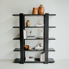 a book shelf with vases and books on it in front of a white wall