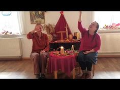 two women sitting at a table with candles in front of them and one holding her hands up