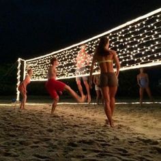 some people are playing volleyball on the beach at night with lights strung up behind them